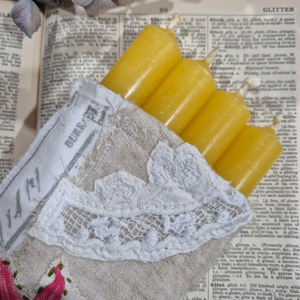 Four  beeswax yellow candles on a textured surface with lace and newspaper