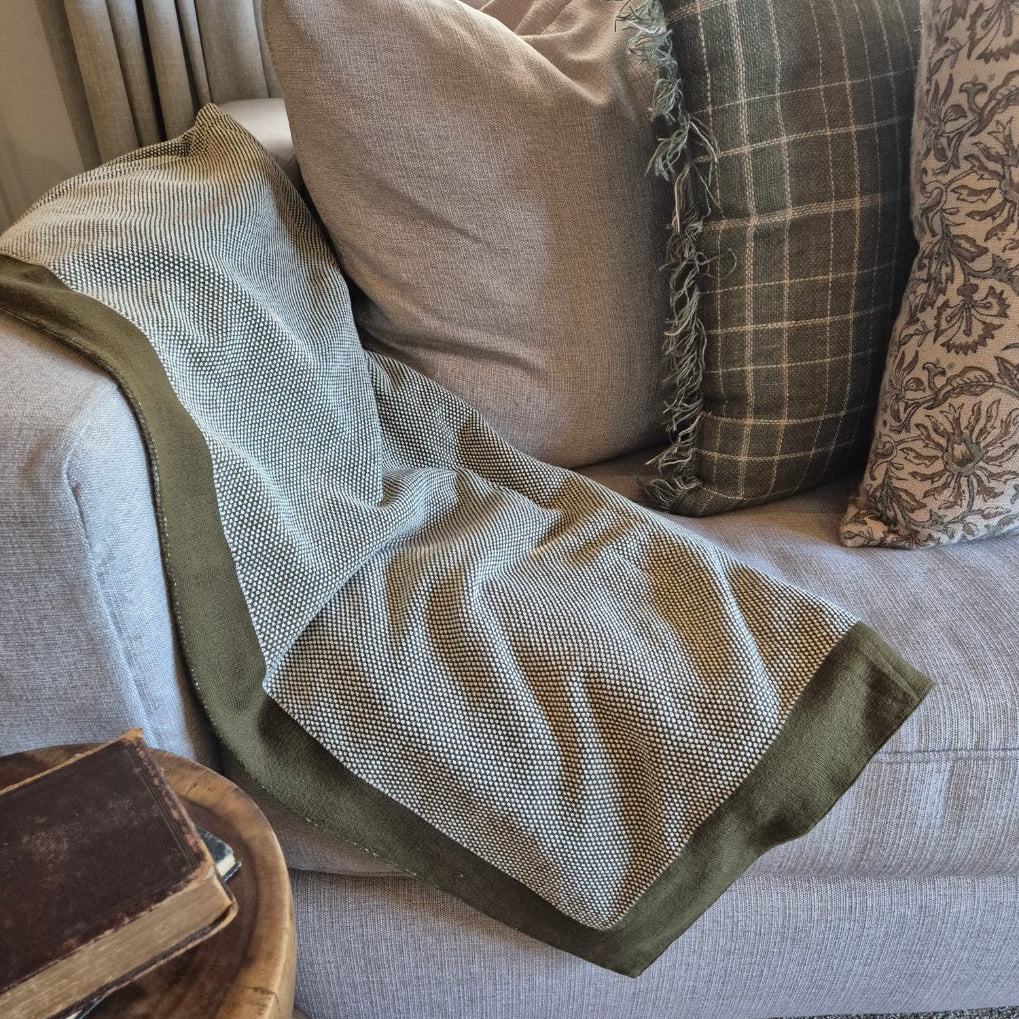 Green blanket draped over a sofa with patterned cushions