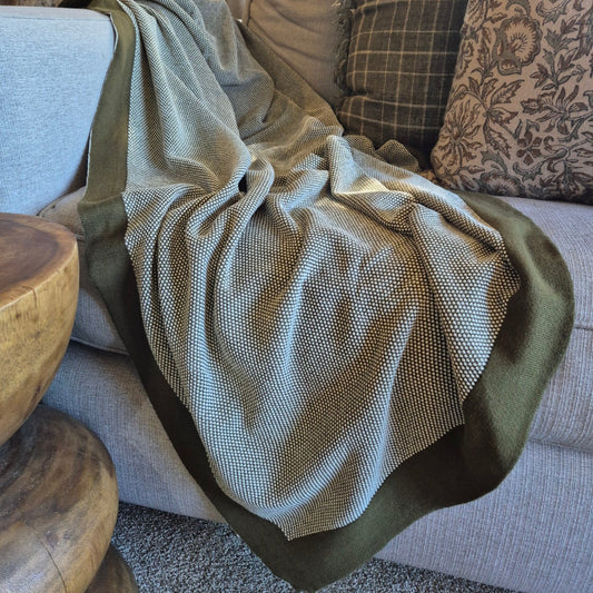 Green blanket draped over a gray sofa with patterned cushions and a wooden side table.