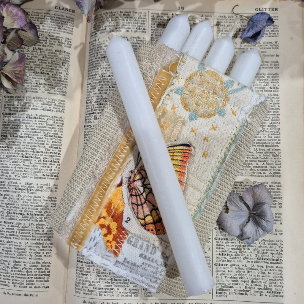Decorative item with a white candle and fabric on an open book with newspaper pages.