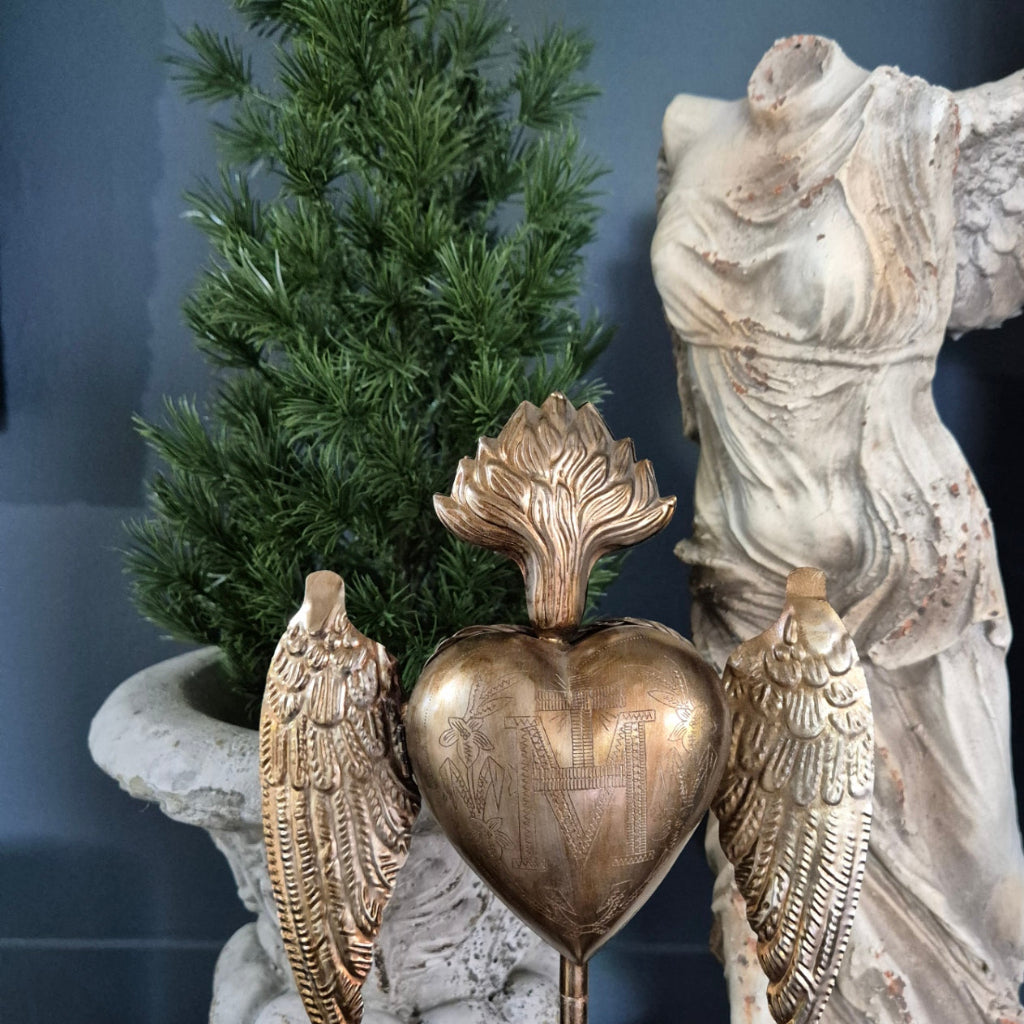 Decorative heart with wings and angel statue against a blue wall