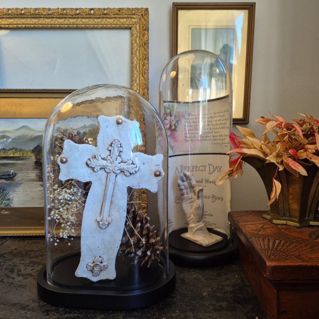 Decorative cross in a glass dome with framed pictures and a wreath in the background