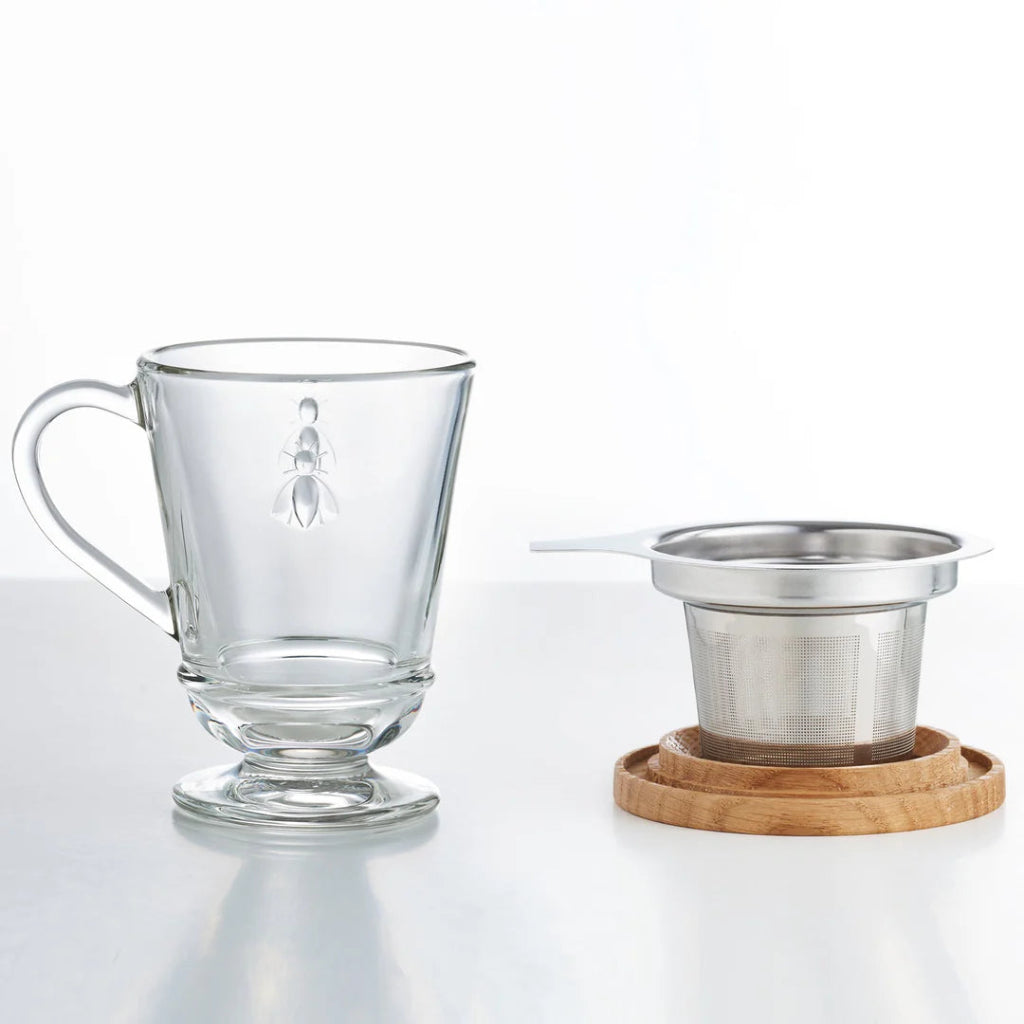 French Bee Clear glass mug with a metal tea infuser on a wooden coaster on a white background