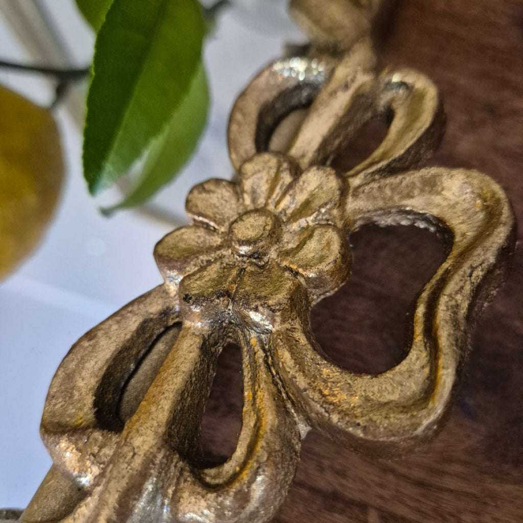 Decorative gold metal handle with floral design on a wooden surface