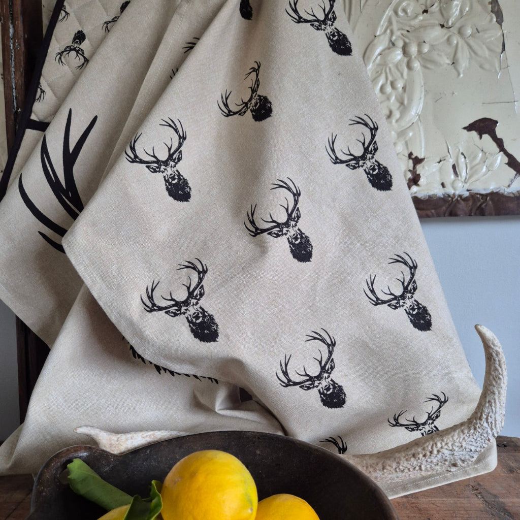 Fabric with black deer skull pattern on a beige background, placed on a wooden surface with a decorative bowl.