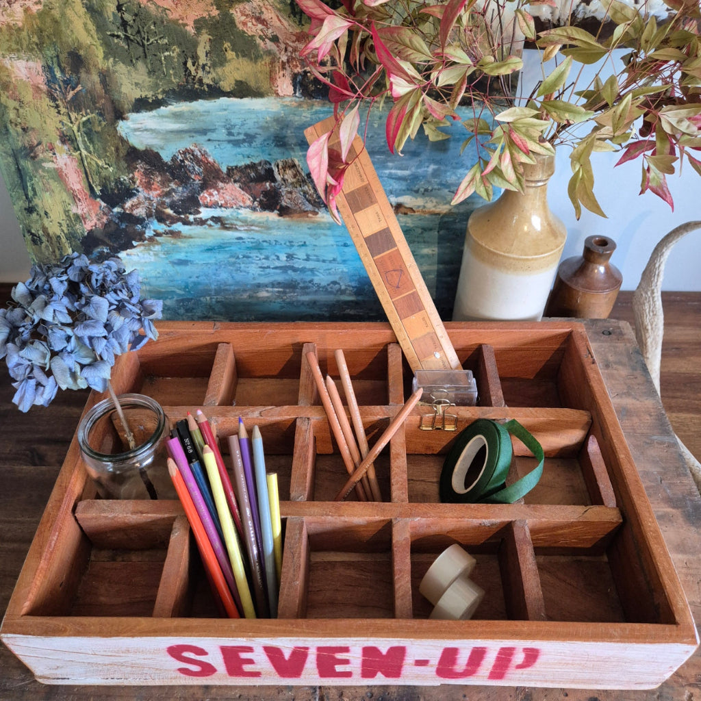 Wooden desk organizer with stationery items next to a plant and artwork.
