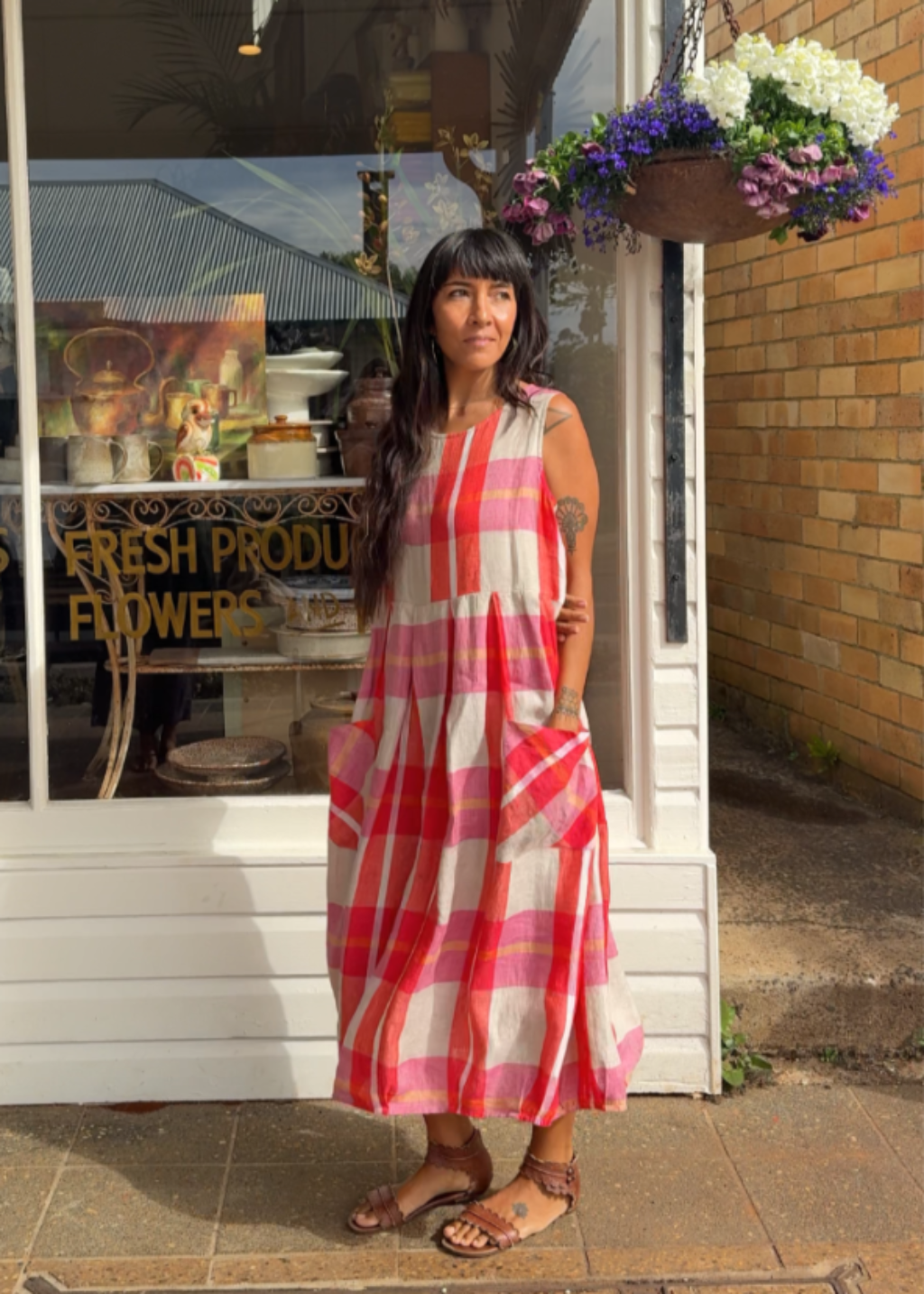 Woman in a red and white checkered dress standing outside a store with flowers above the door.