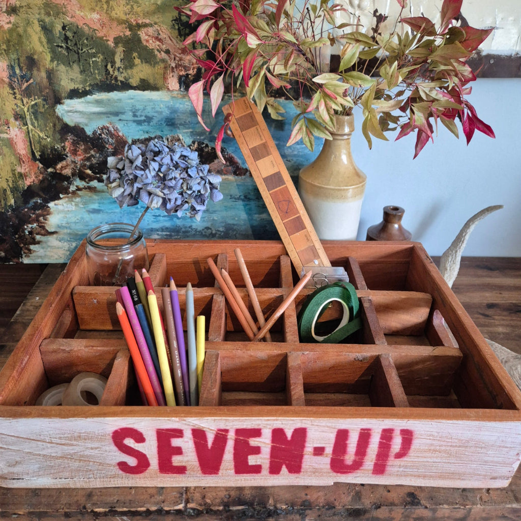Wooden box tray with stationery items and 'SEVEN UP' branding against a rustic background.