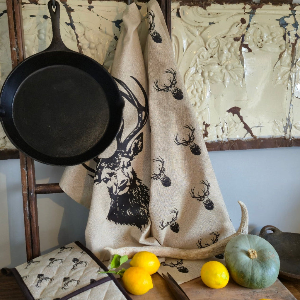 Set of kitchen towels and oven mitts with black designs on a wooden surface.
