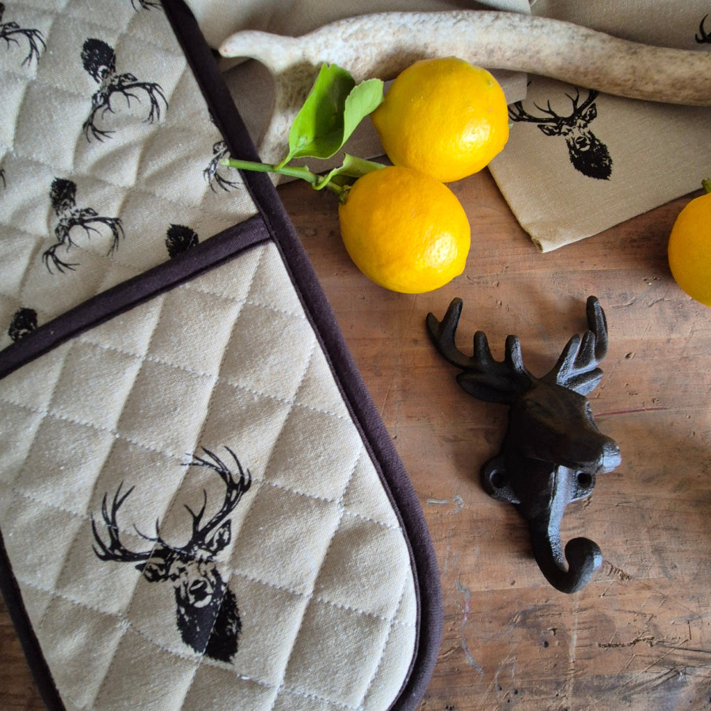 Potholder with deer design on a wooden surface with lemons and a towel.