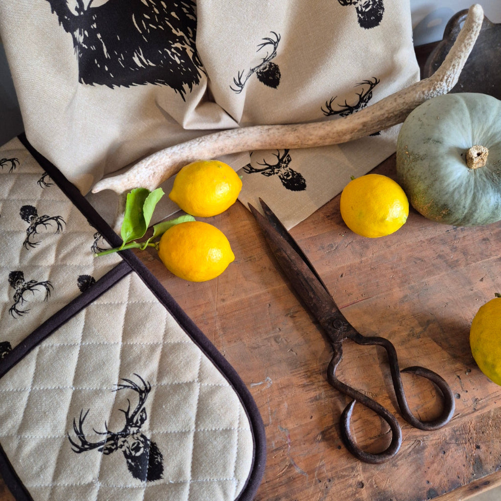 Decorative kitchen items including a towel, oven mitt, and shears on a wooden surface with lemons and a pumpkin.