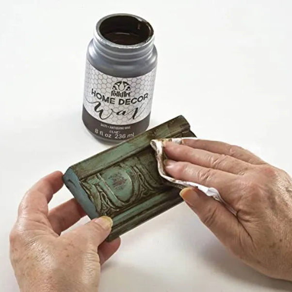 Person applying home decor wax to a wooden block with a can of wax labeled 'Home Decor Wax' in the background.