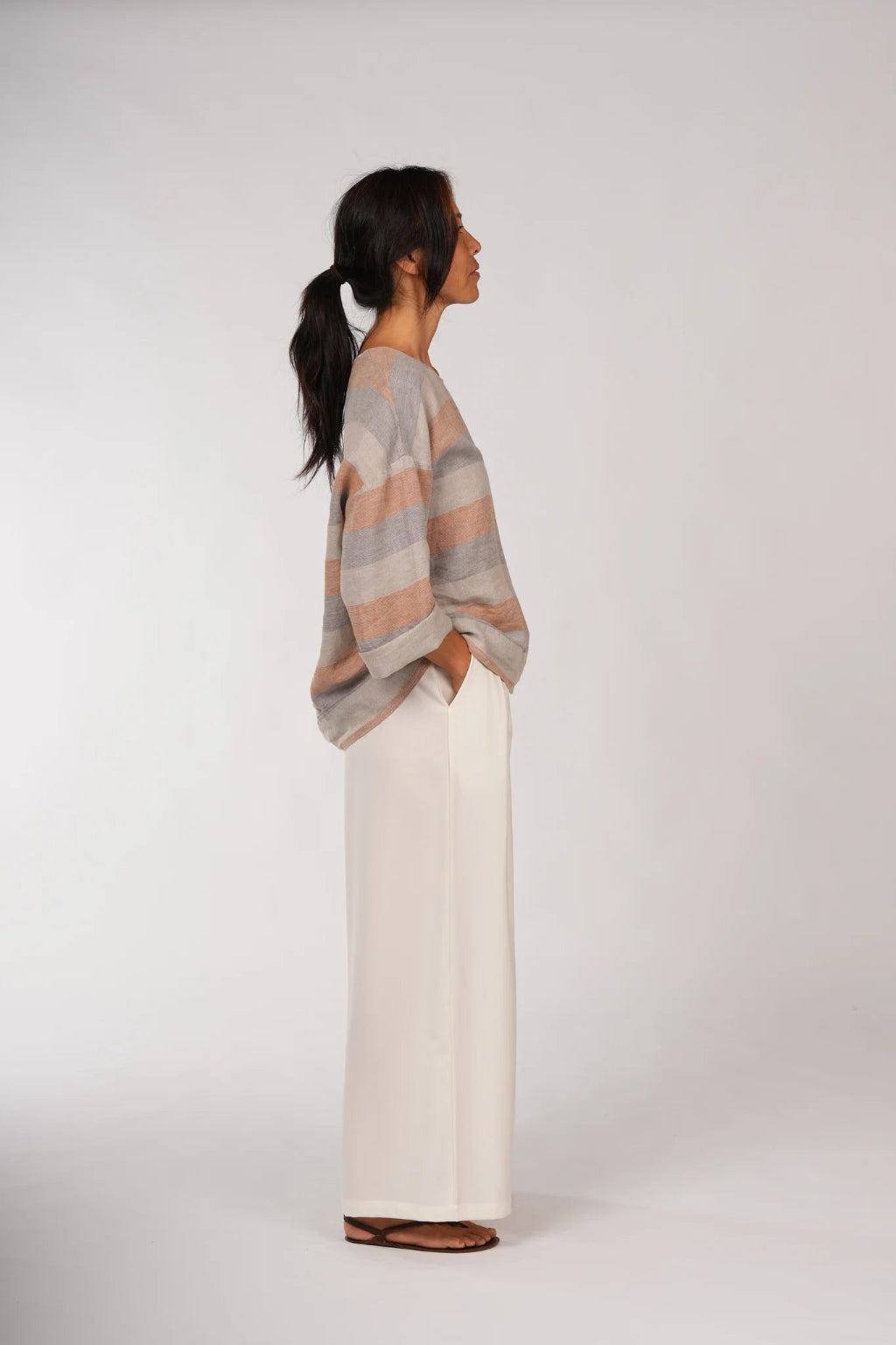Woman wearing a striped sweater and white pants on a white background