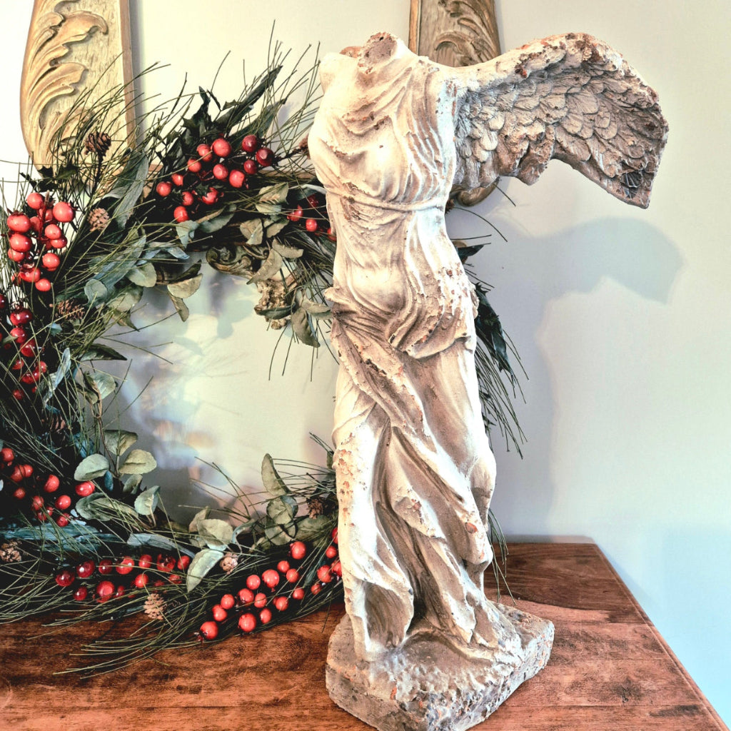 Statue of a winged figure next to a decorative wreath with berries on a wooden surface.