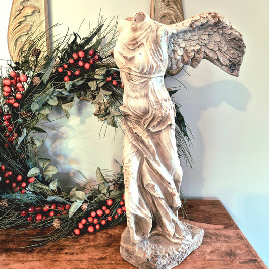 Statue of a winged figure next to a decorative wreath with berries on a wooden surface.