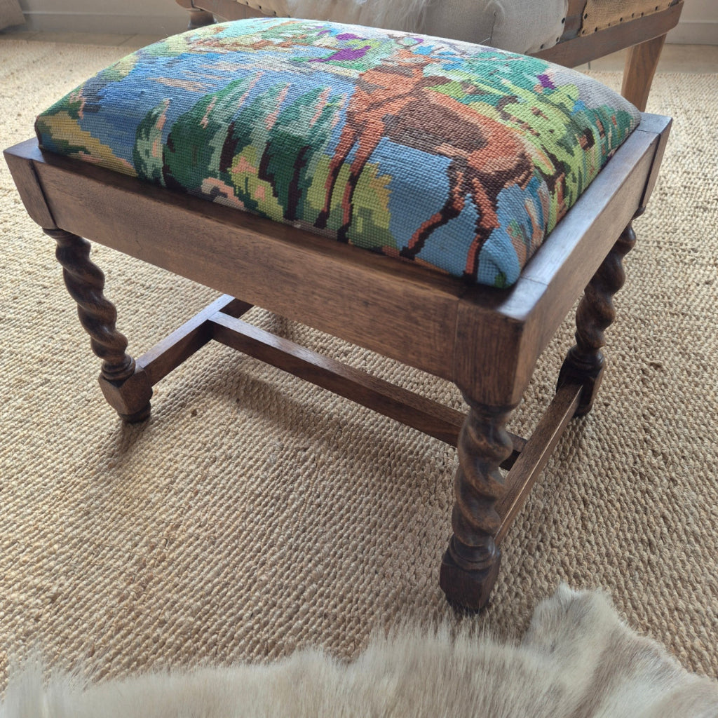 Oak stool with a colorful needlepoint cushion on a carpeted floor