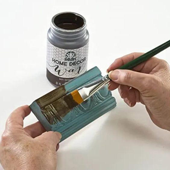 Person holding a paintbrush over a container of antique wax 
