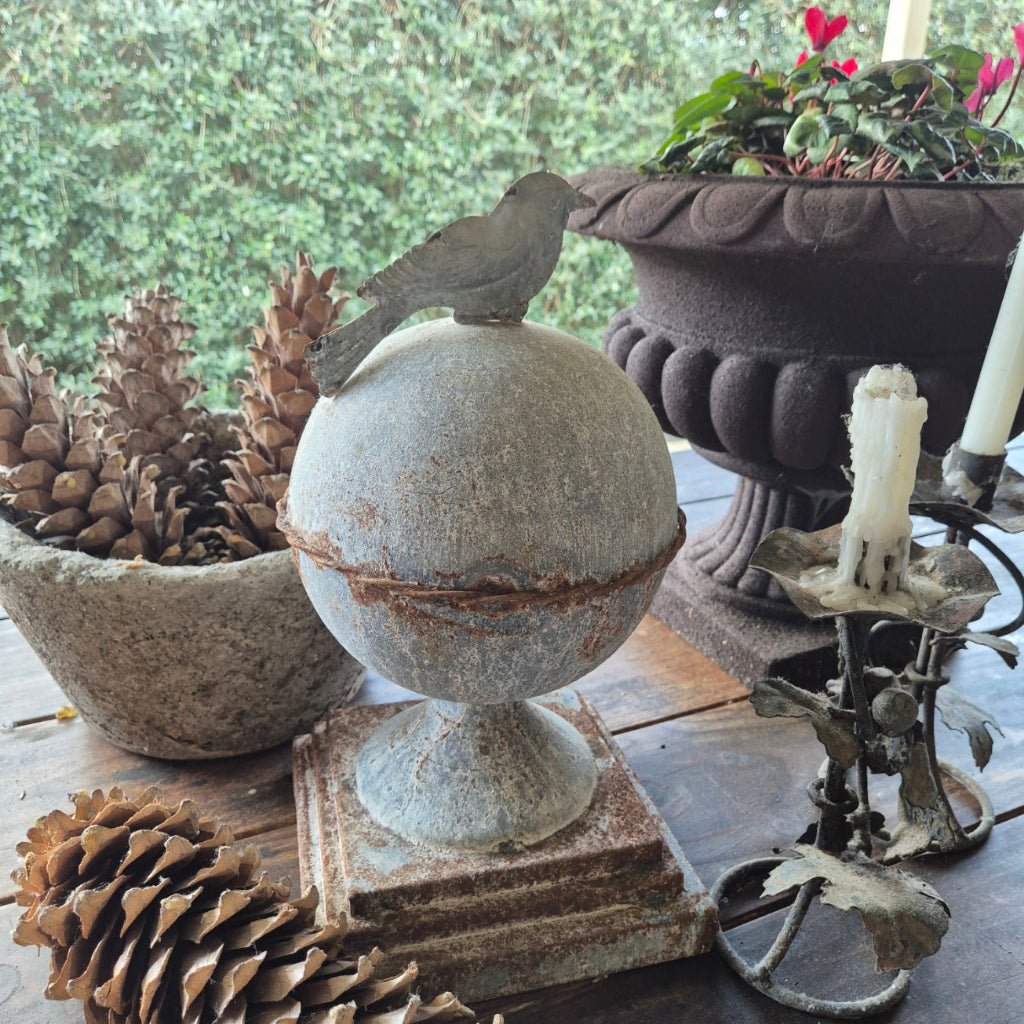 Decorative arrangement with iron bird obelisk , pinecones, and a metal candlesticks