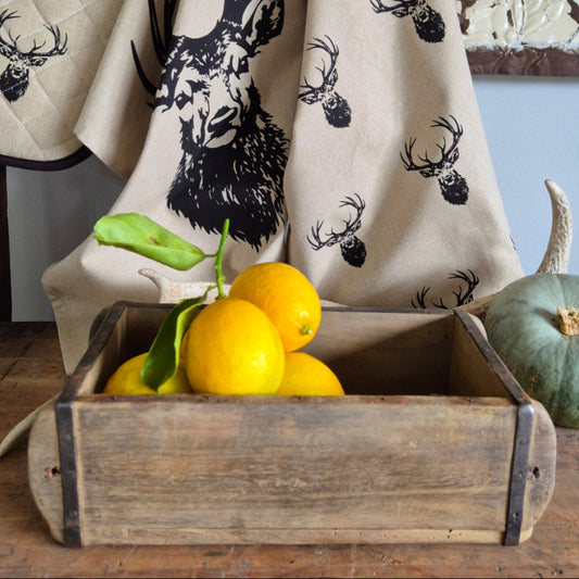 Beige fabric with black deer pattern on a wooden surface with lemons and a green pumpkin next a brick mould