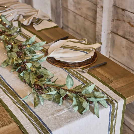 Decorative Christmas table setting with greenery and white plates on a wooden table.