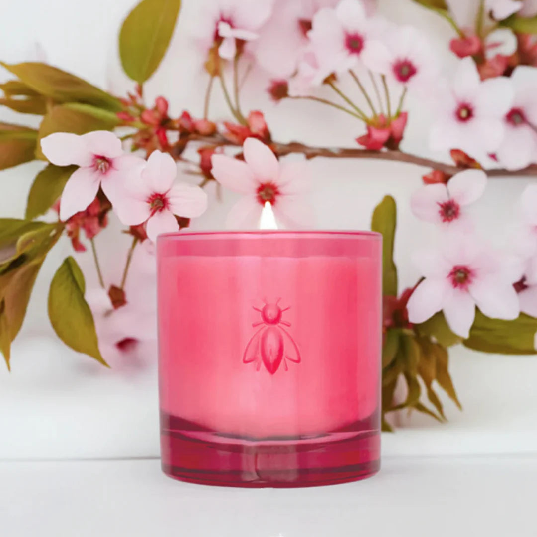 Pink candle with a bee logo in front of cherry blossoms