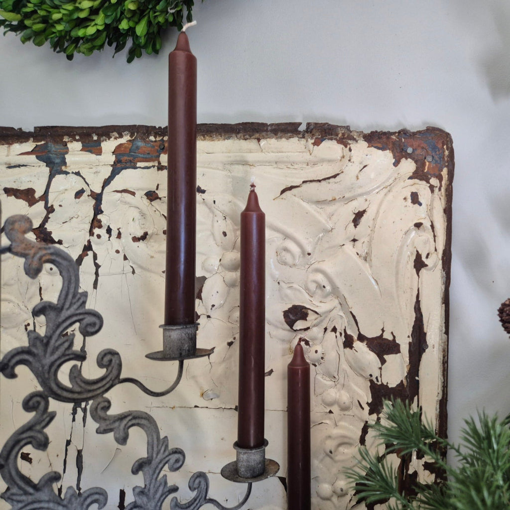 Three brown candles on a decorative metal candelabra against a textured wall.