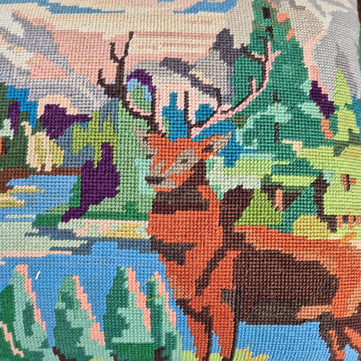 Close-up of a needlepoint or cross-stitch piece depicting a forest scene with trees and animals.