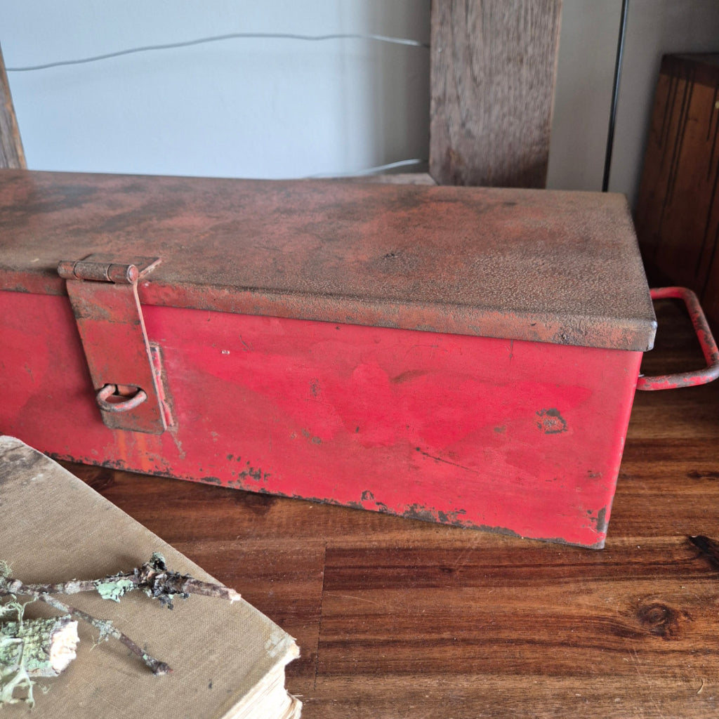 Rust-colored metal box with a red top against a wooden wall.