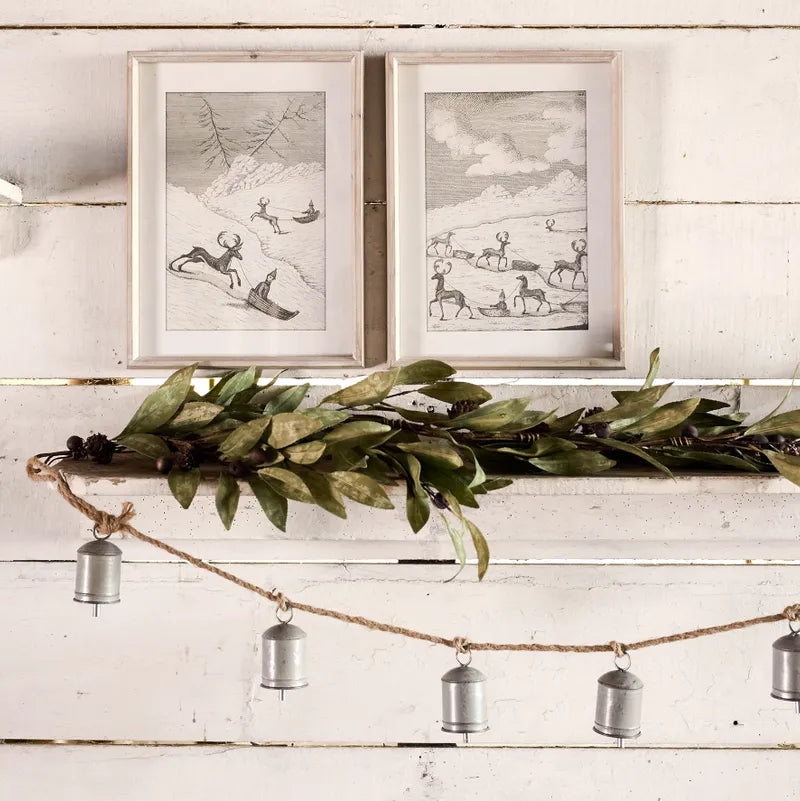 Decorative shelf with greenery, metal pendants, and framed artwork on a wooden wall.
