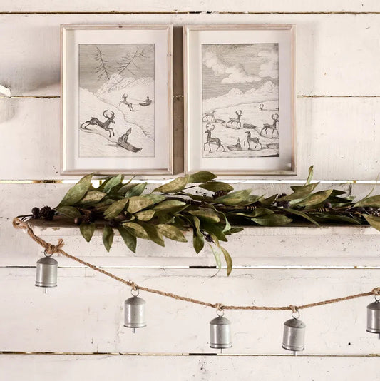 Decorative shelf with greenery, metal pendants, and framed artwork on a wooden wall.