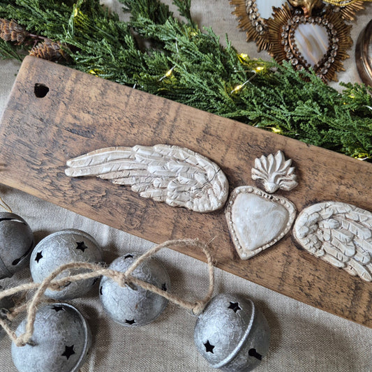 Decorative angel wings and bells on a wooden board with greenery and lights in the background