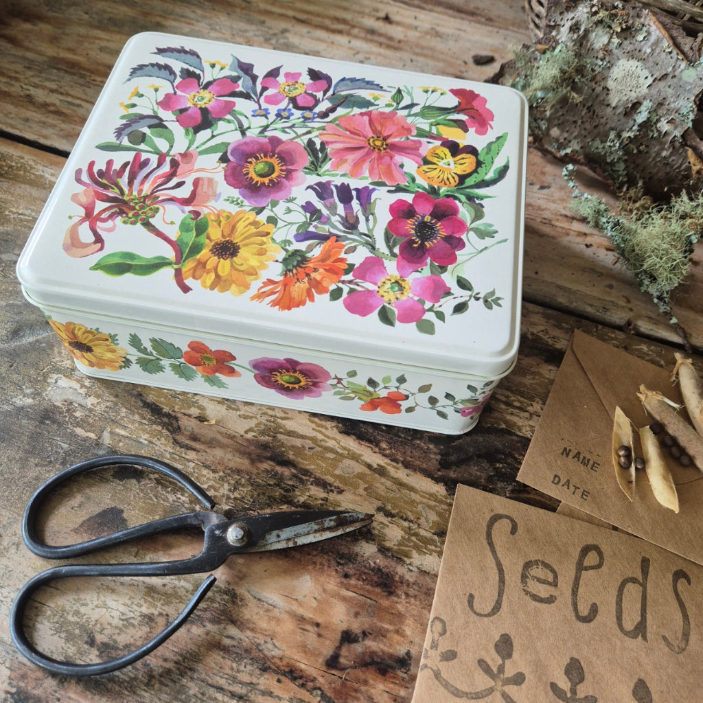 Floral-patterned seed tin on a wooden surface with scissors and paper.