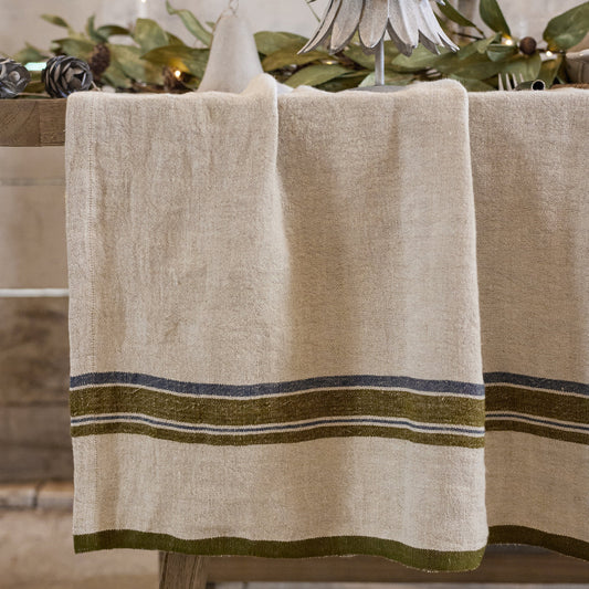 Beige Linen tablecloth with green stripes on a wooden table, set against a stone wall.