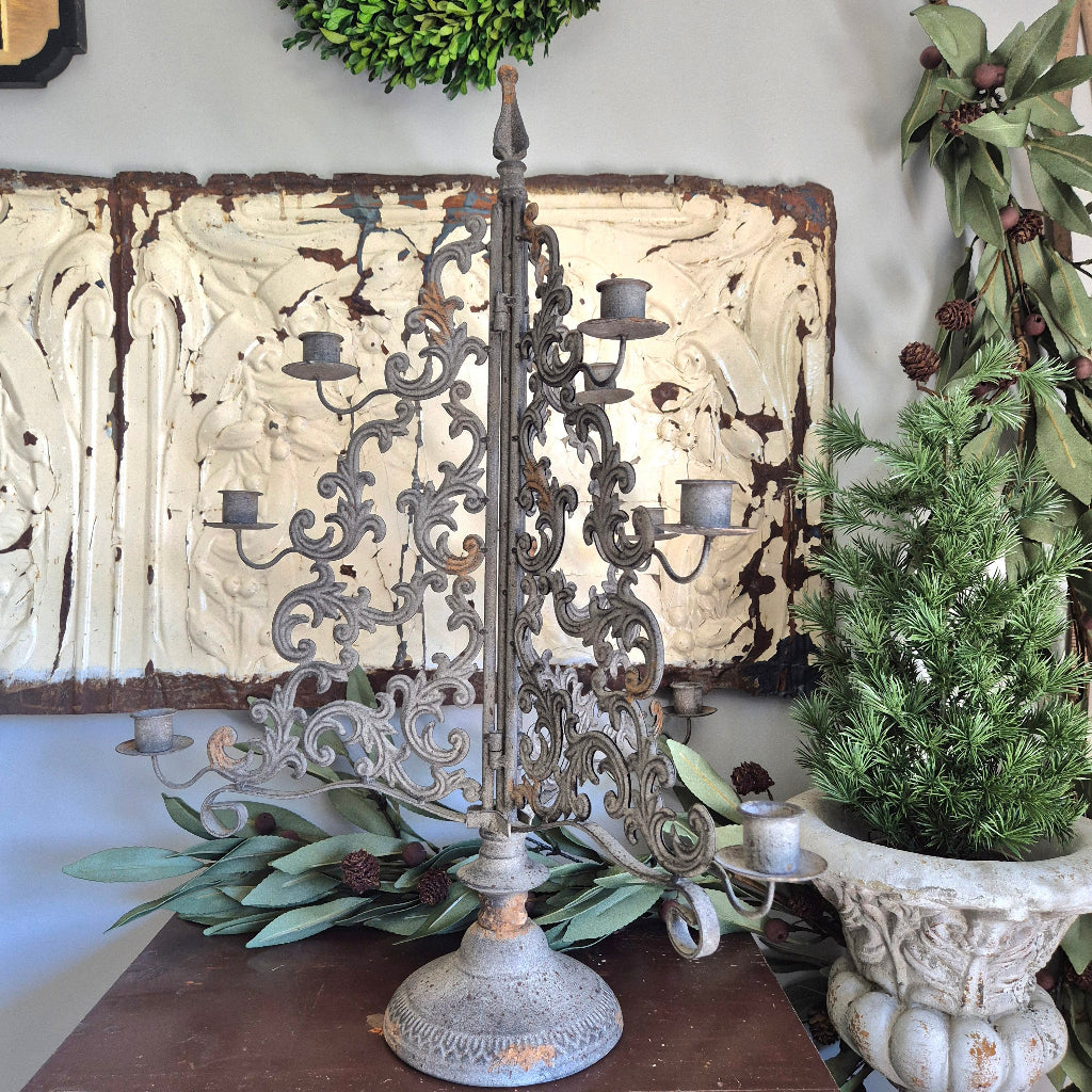 Decorative metal candelabra with candles on a table against a decorative wall.