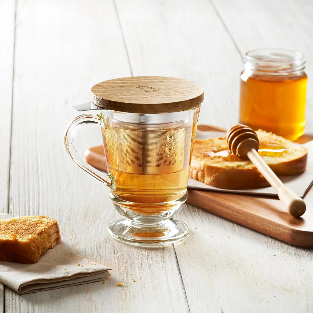 Clear glass Abeille mug with wooden lid on a wooden table with toast and honey