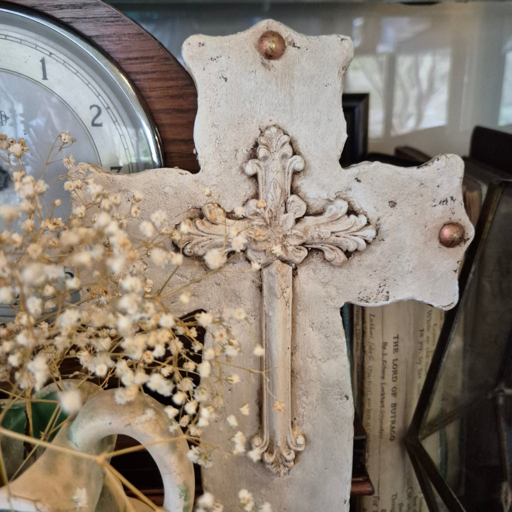 Decorative cross with intricate details and dried flowers in front of a clock.
