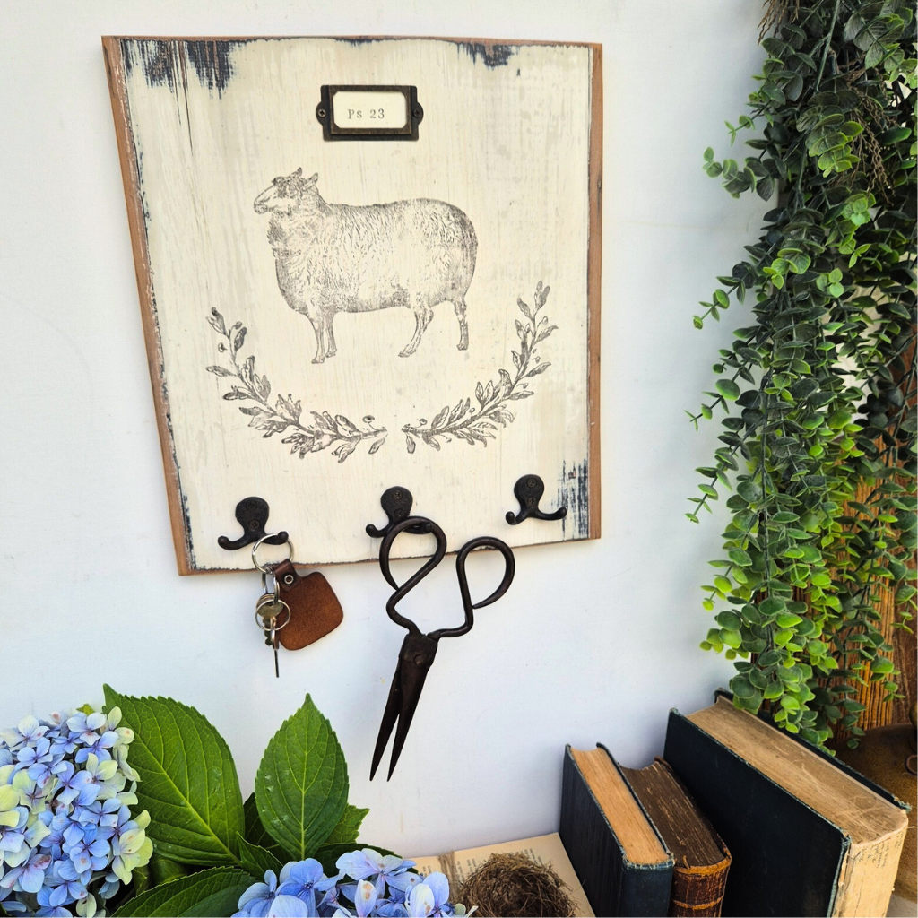 Decorative wall hook with sheep design, scissors, and keys on a white wall with plants and books.