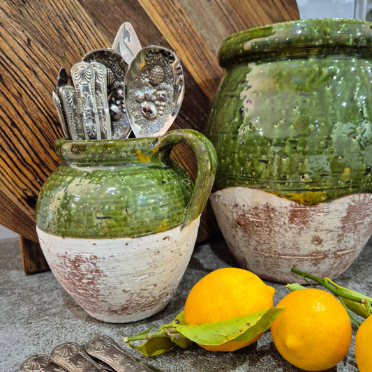 Green ceramic jar with silver spoons and lemons on a wooden surface