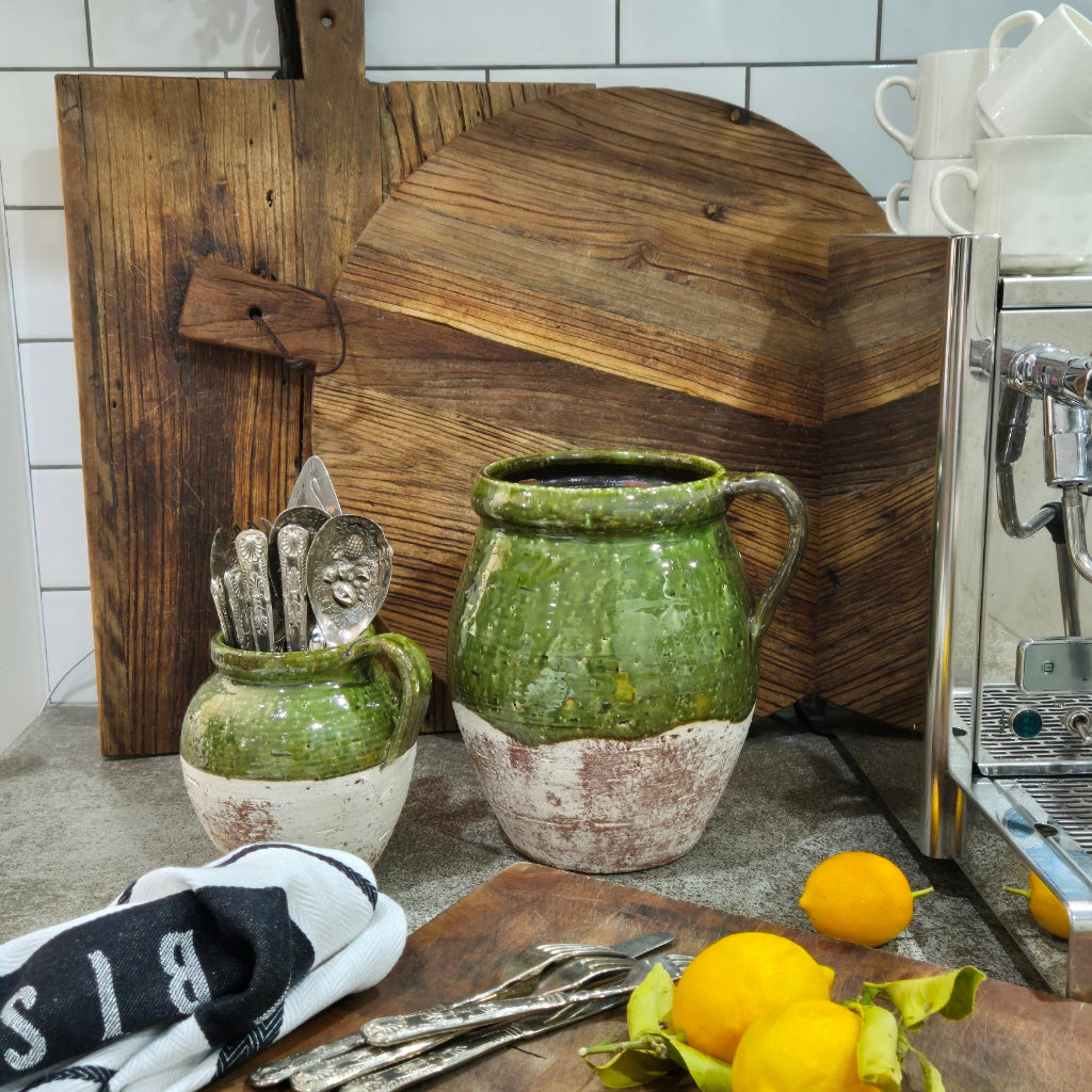 Two green ceramic pots on a wooden surface with a kitchen sink in the background.