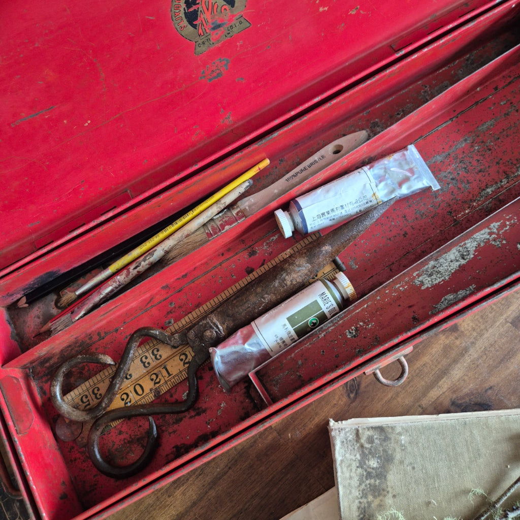 Vintage tools including a tube of paint, ruler, and scissors inside a red toolbox.