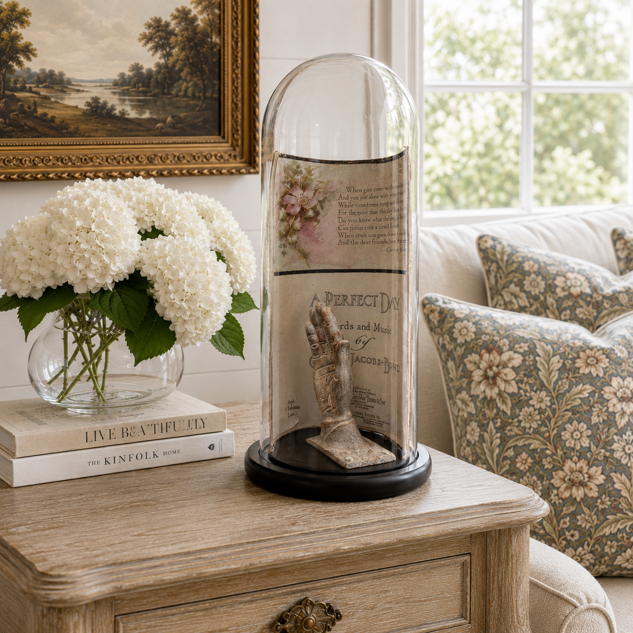 Decorative display with a figurine in a glass dome on a wooden table, surrounded by books and flowers.