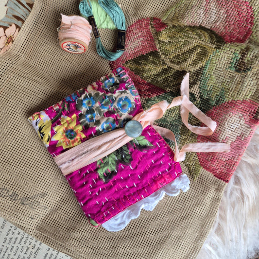 Decorative fabric pouch with floral patterns and a pink ribbon on a textured surface.