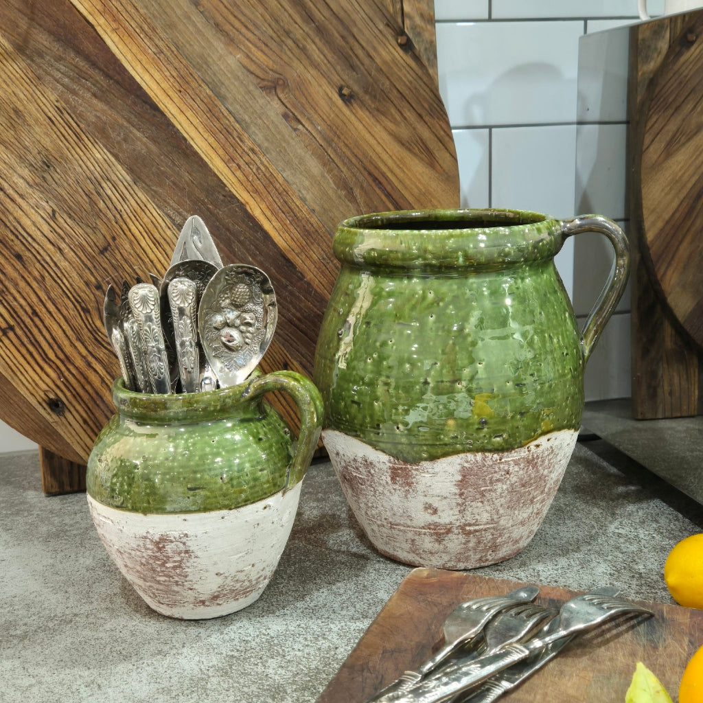 Two green ceramic pots with handles on a wooden surface.