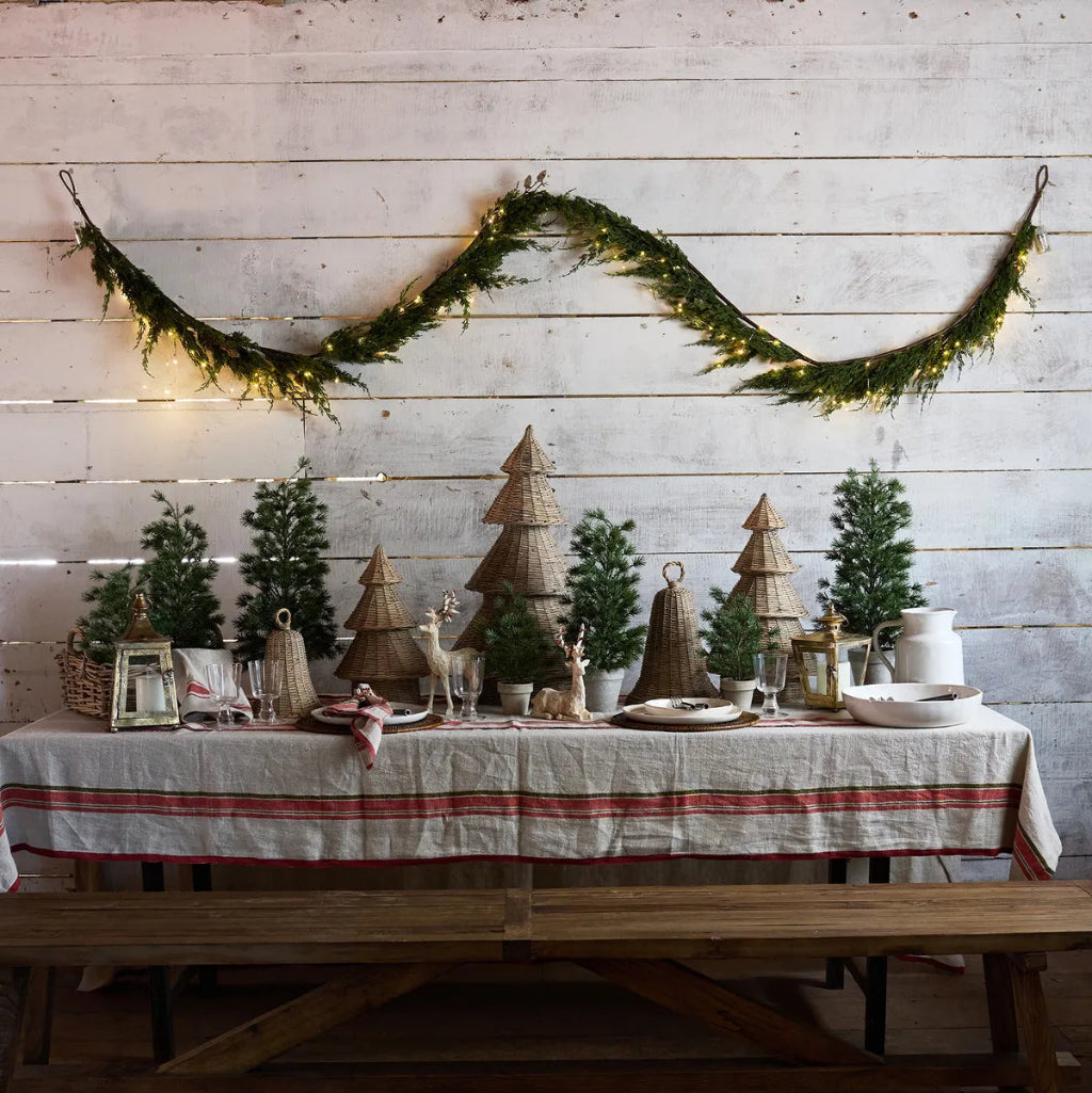 Decorated table with Christmas trees and lights against a wooden wall.