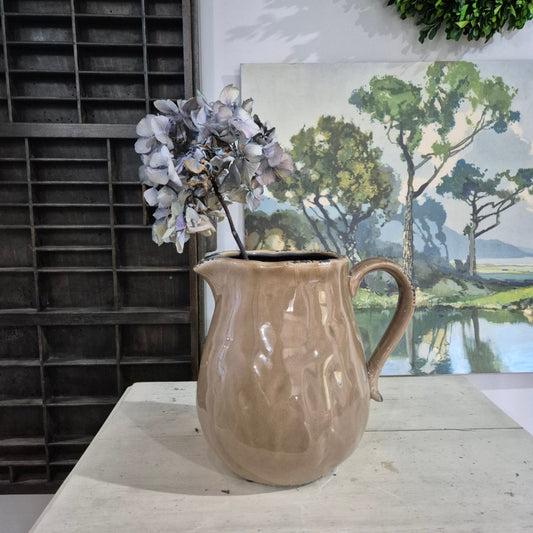 Brown ceramic mug on a white surface with a blurred painting in the background