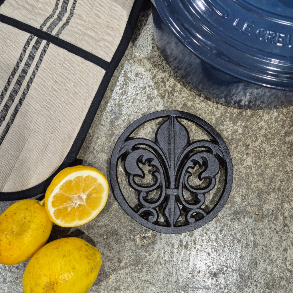 Decorative black cast iron trivet with a floral design on a stone surface with lemons.