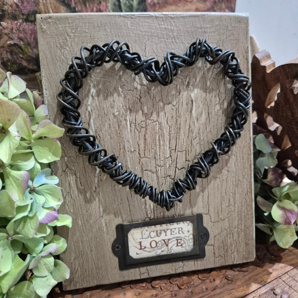 Black wire heart on a rustic wooden surface with green flowers