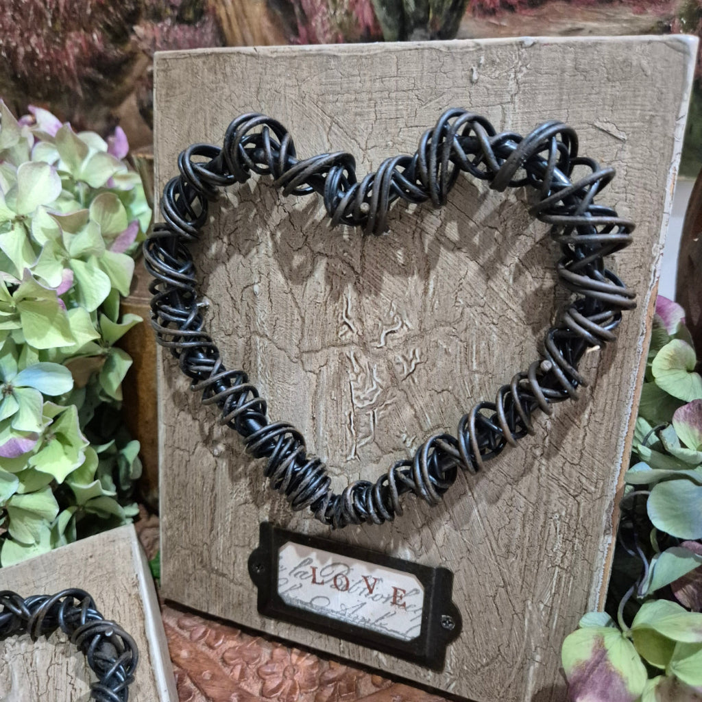 Black braided heart on a textured wooden surface with a 'LOVE' tag.