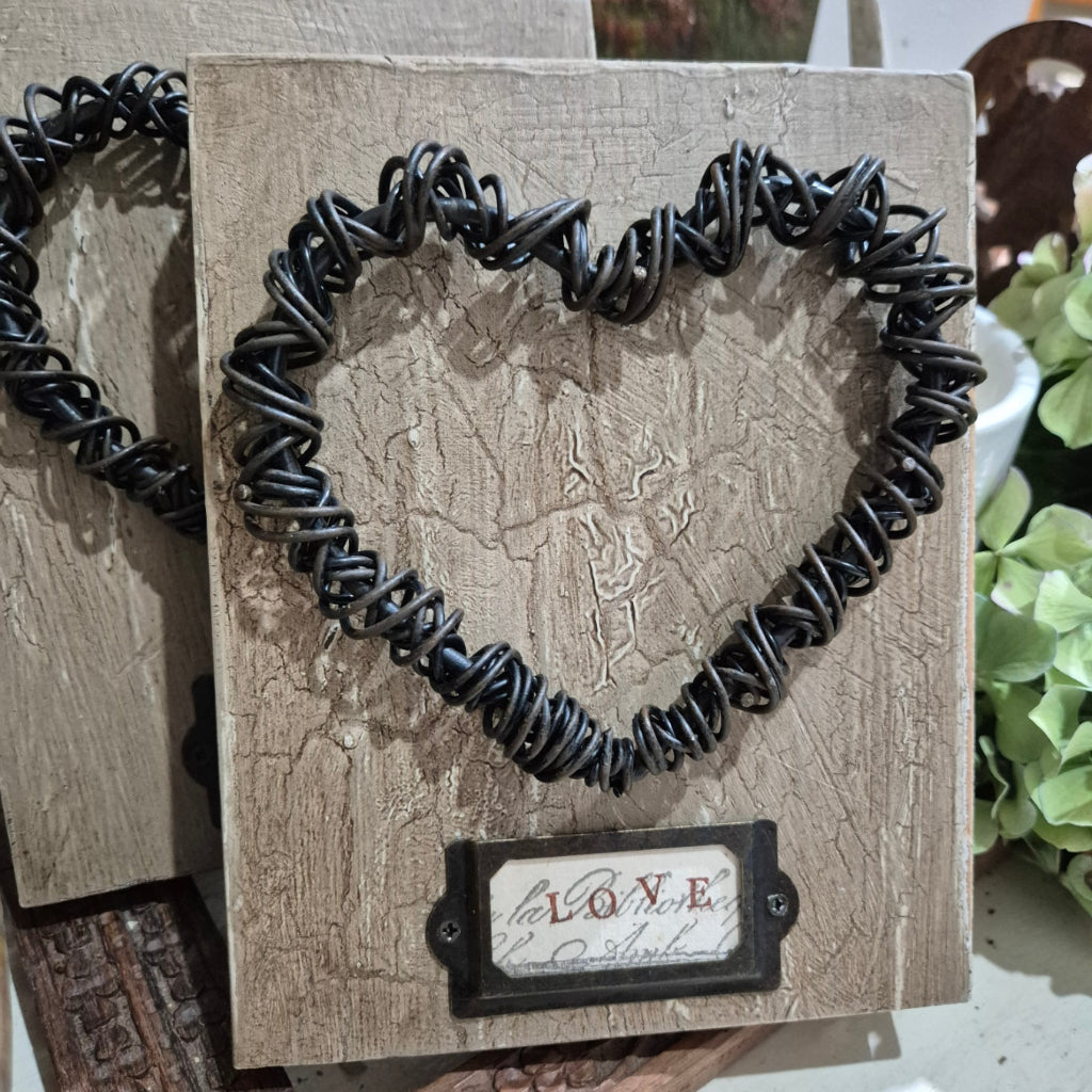 Black wire heart on a textured wooden block with 'LOVE' tag