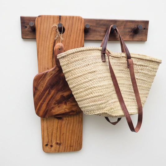 Wooden wall hook with a woven basket and wooden cutting board on a white background